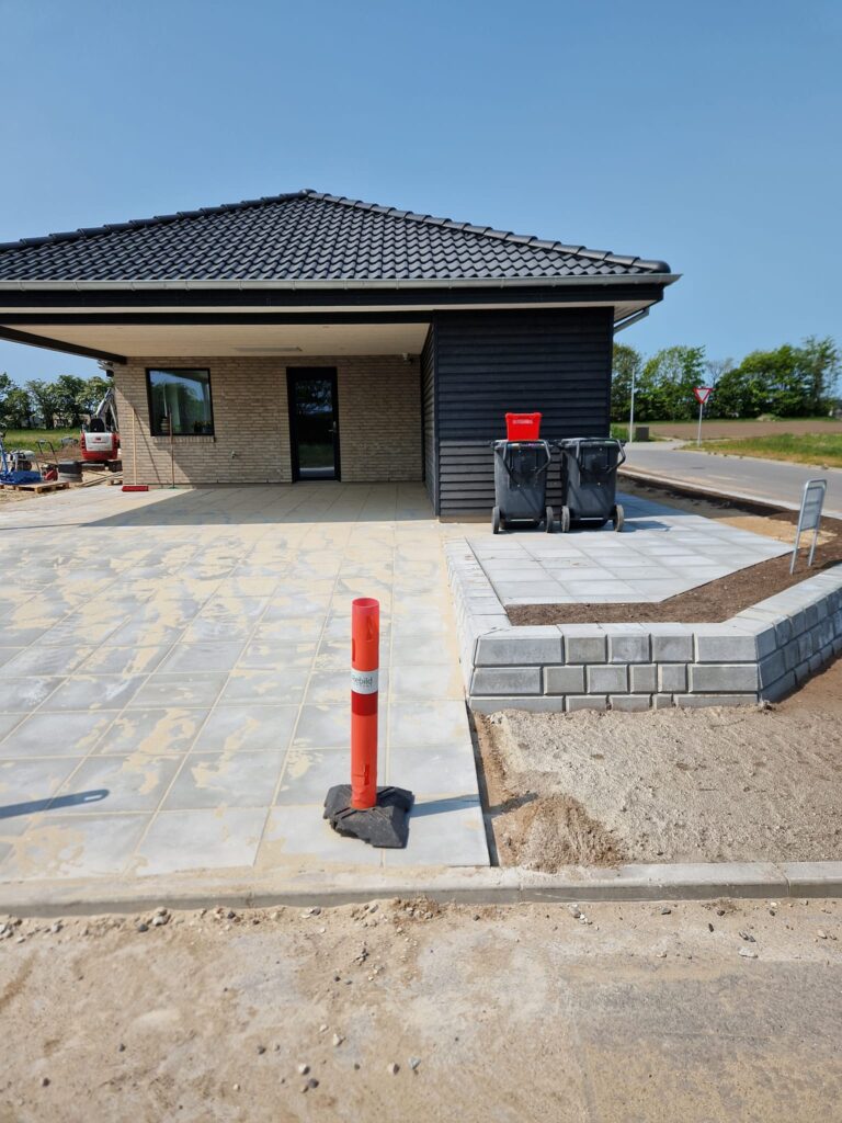 Nybygget hus med flisebelagt indkørsel og affaldscontainere